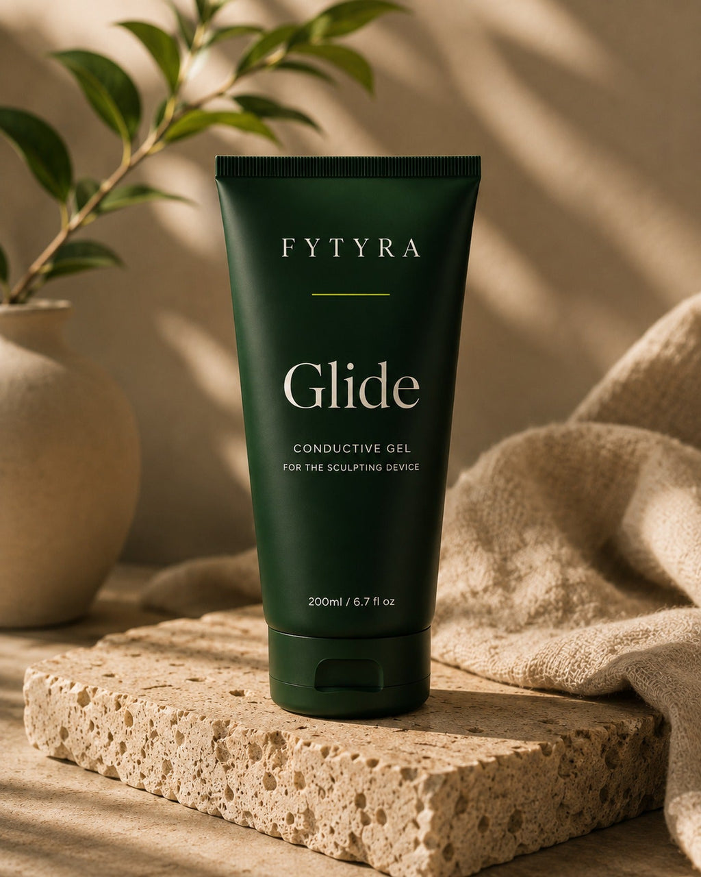 Fytyra Glide conductive gel, a 200ml deep green tube, standing on travertine beside linen